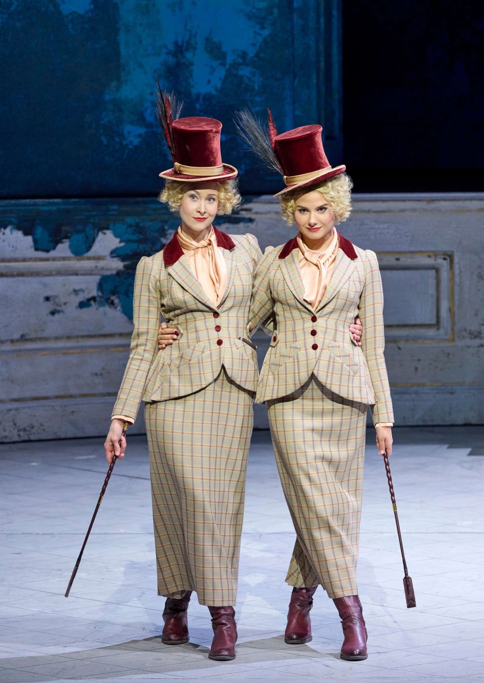 Zwei identisch gekleidete Frauen mit gestreiften Kostümen und roten Zylindern stehen Arm in Arm und halten Spazierstöcke.