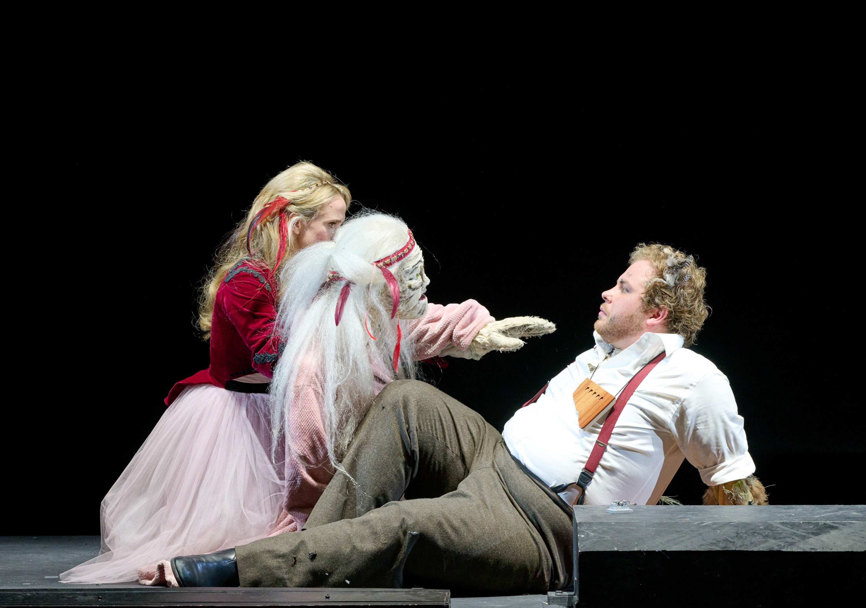 Ein Mann mit einer Panflöte um den Hals liegt halb auf dem Boden. Ihm gegenüber sitzt eine junge Frau, die eine Handpuppe vor sich hält.