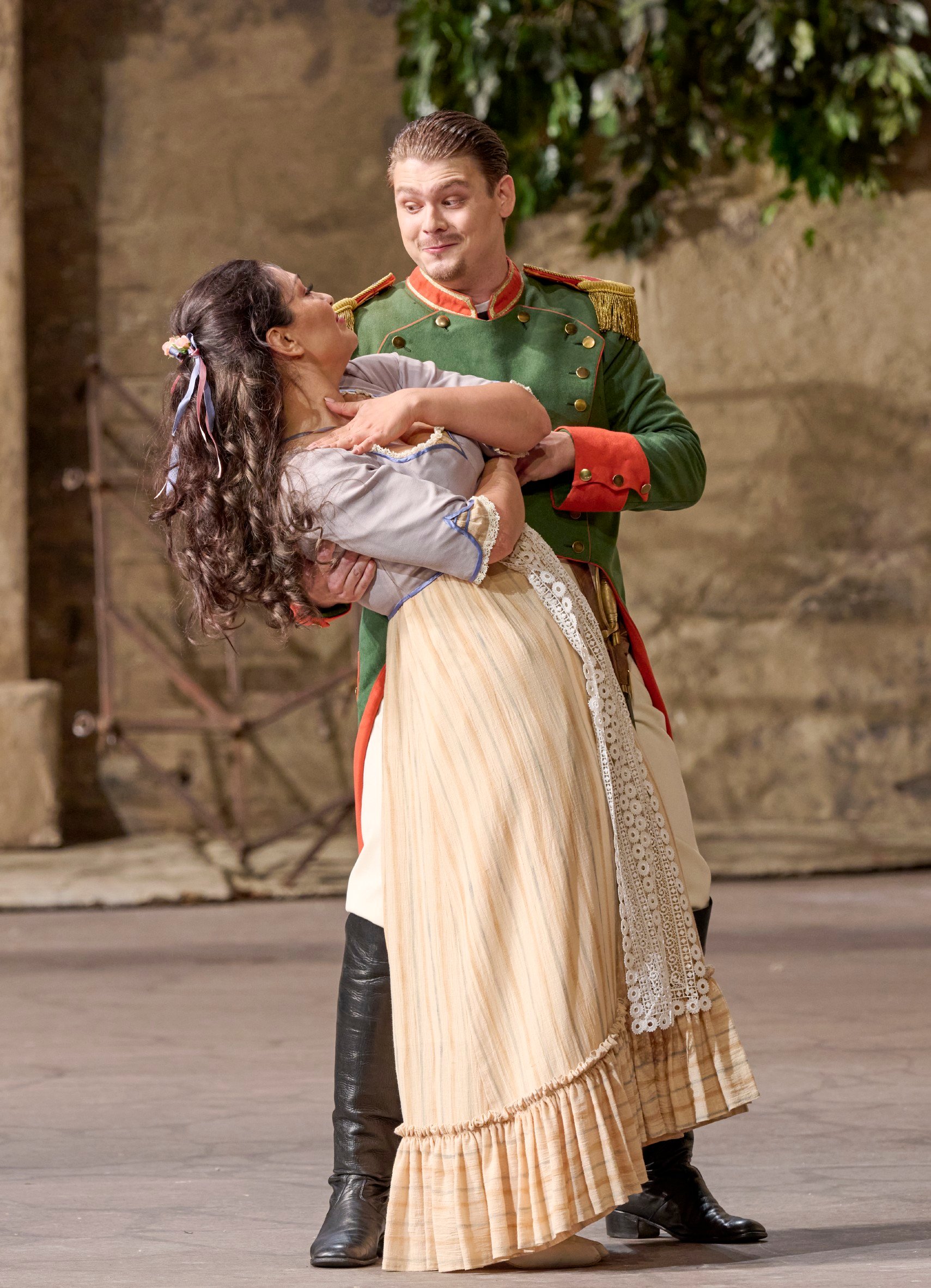 Ein Soldat in grüner Uniform hält eine lachende Frau im Arm in einer romantischen Bühnenpose.