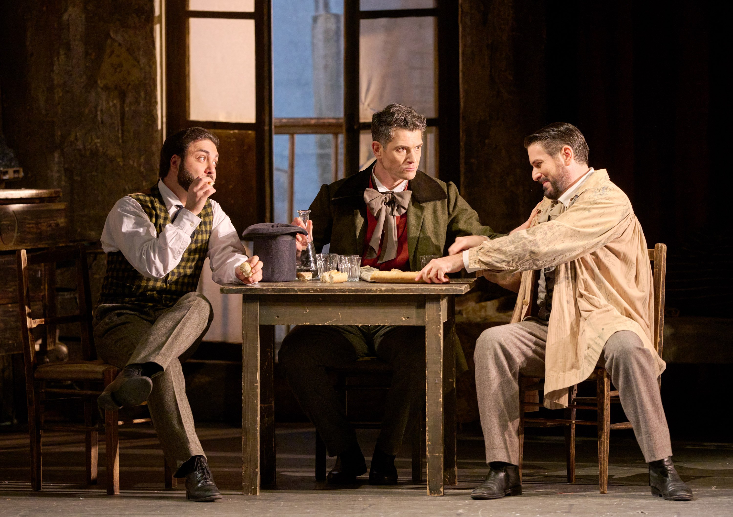 Drei Männer in historischer Kleidung sitzen an einem Tisch, scherzen und teilen sich eine Mahlzeit in geselliger Stimmung.