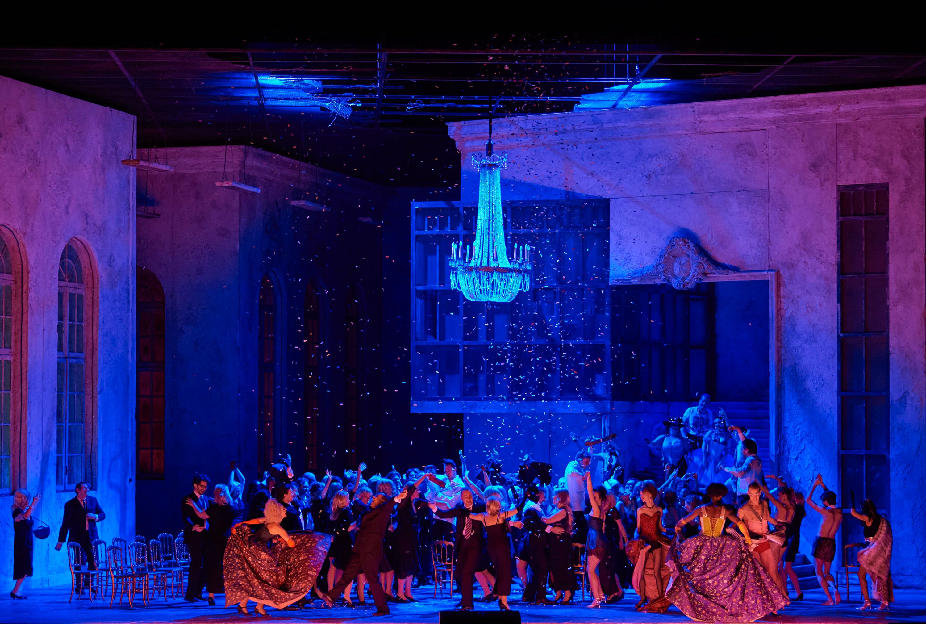 Eine große Menschenmenge feiert und tanzt ausgelassen in einer Bühnenkulisse