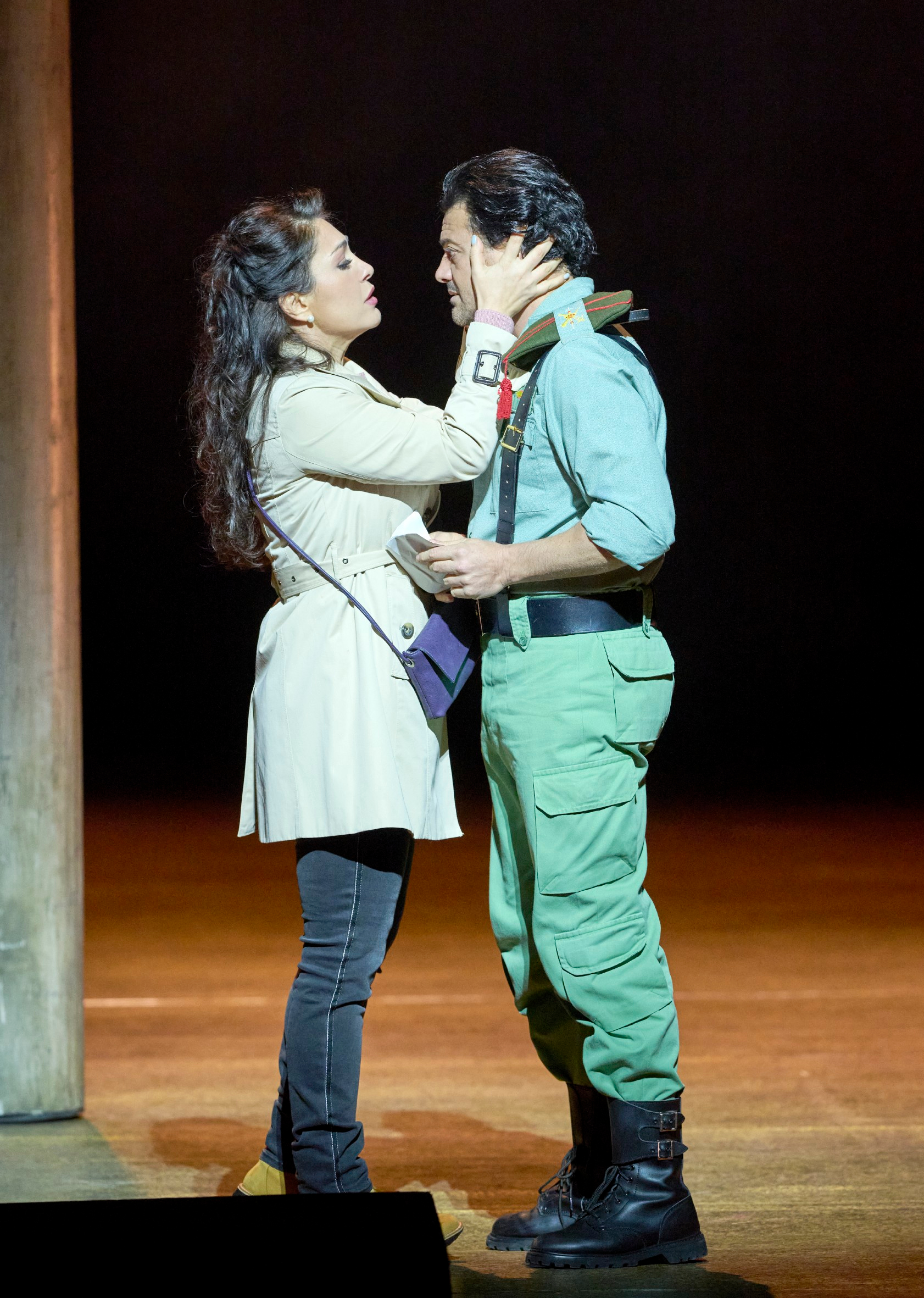 Eine Frau in hellem Mantel berührt sanft das Gesicht eines Mannes in Uniform, während sie sich liebevoll in die Augen sehen.