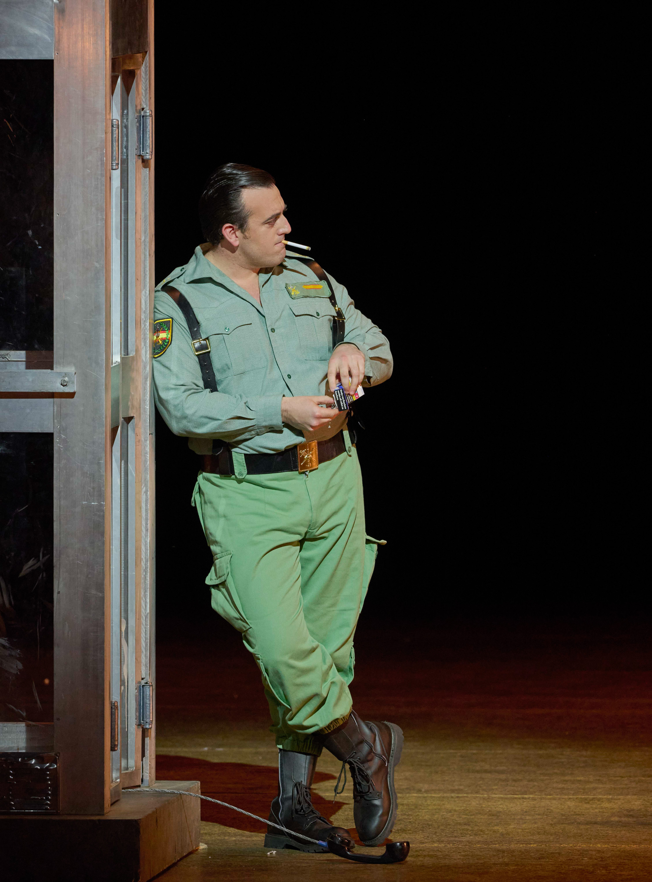 Ein Mann in Uniform lehnt sich an ein Gerüst; er hat eine Zigarette im Mund.