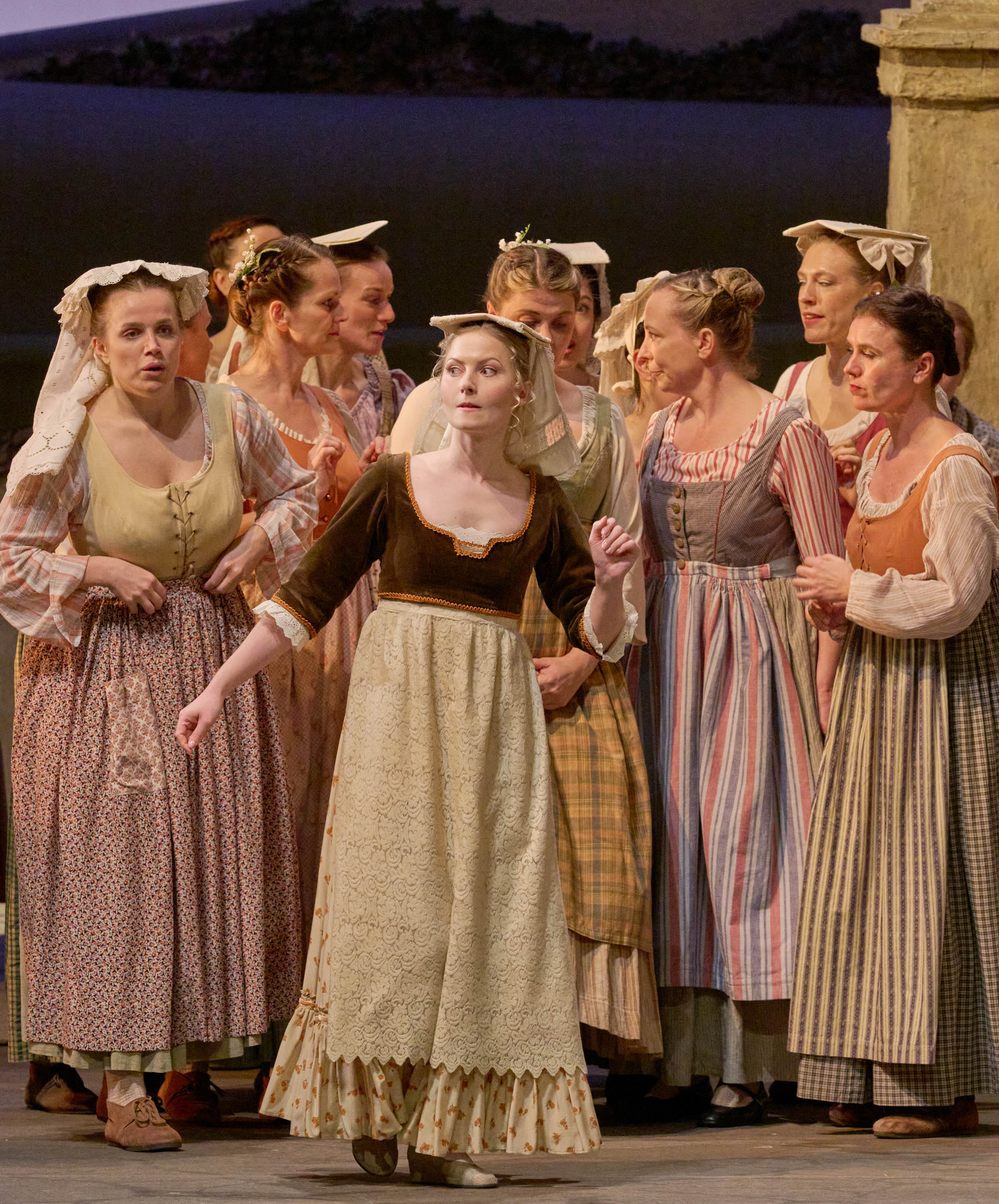 Eine Gruppe von Frauen in historischer Kleidung steht eng beieinander und blickt aufgeregt in eine Richtung auf der Bühne.