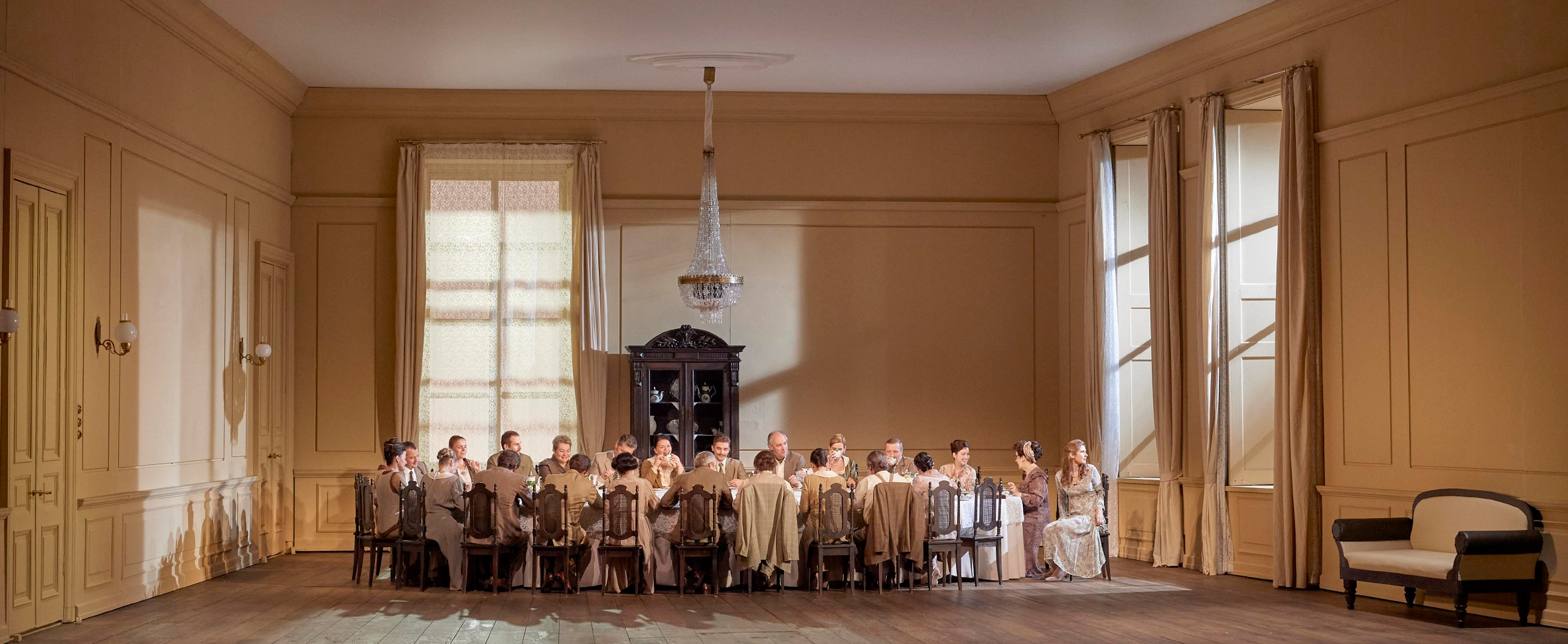 Eine große Gruppe von Personen sitzt in heller Kleidung an einem langen Tisch in einem elegant eingerichteten Raum.