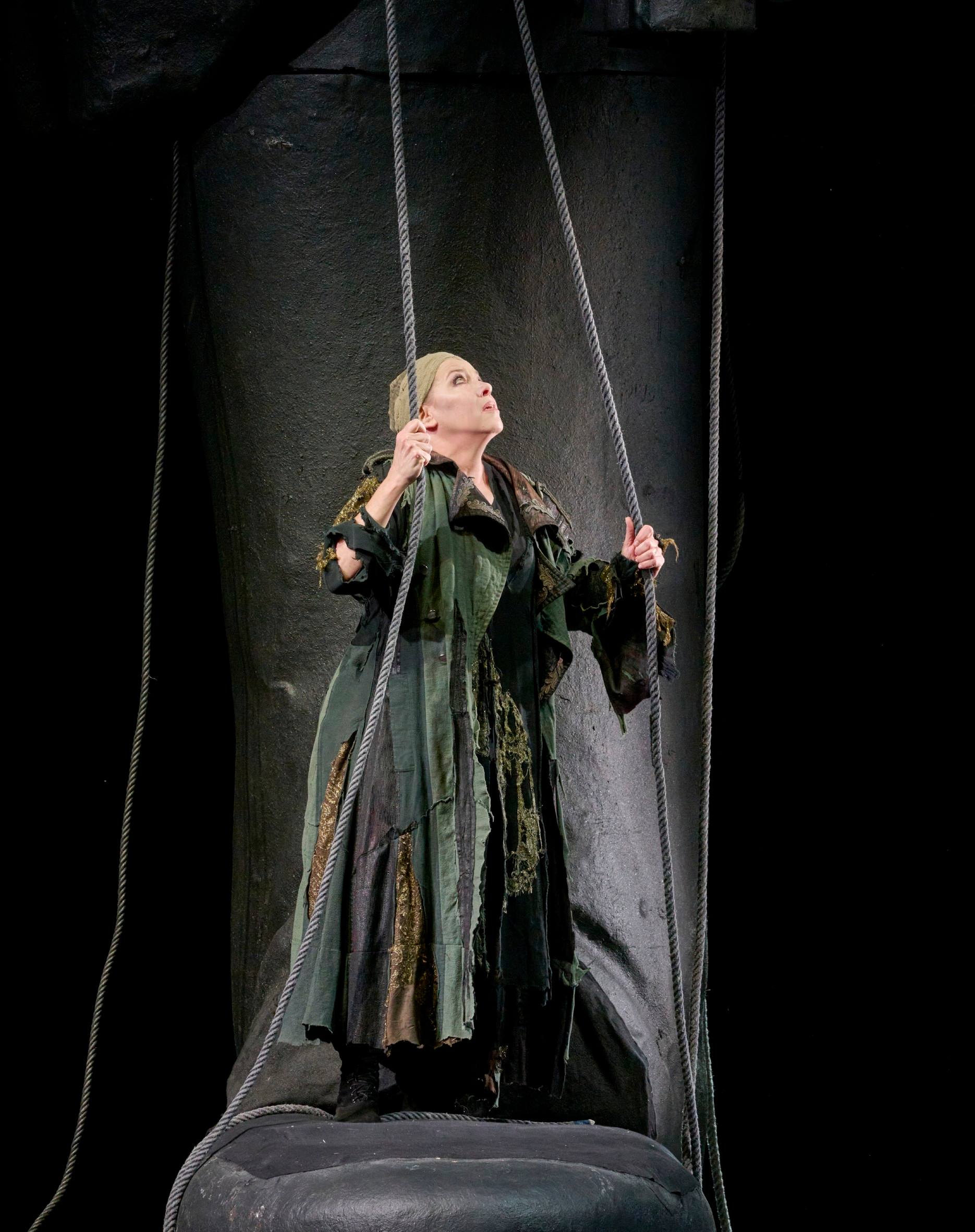 Eine Frau in dunklem Gewand steht auf der Bühne und hält zwei Seile in den Händen.