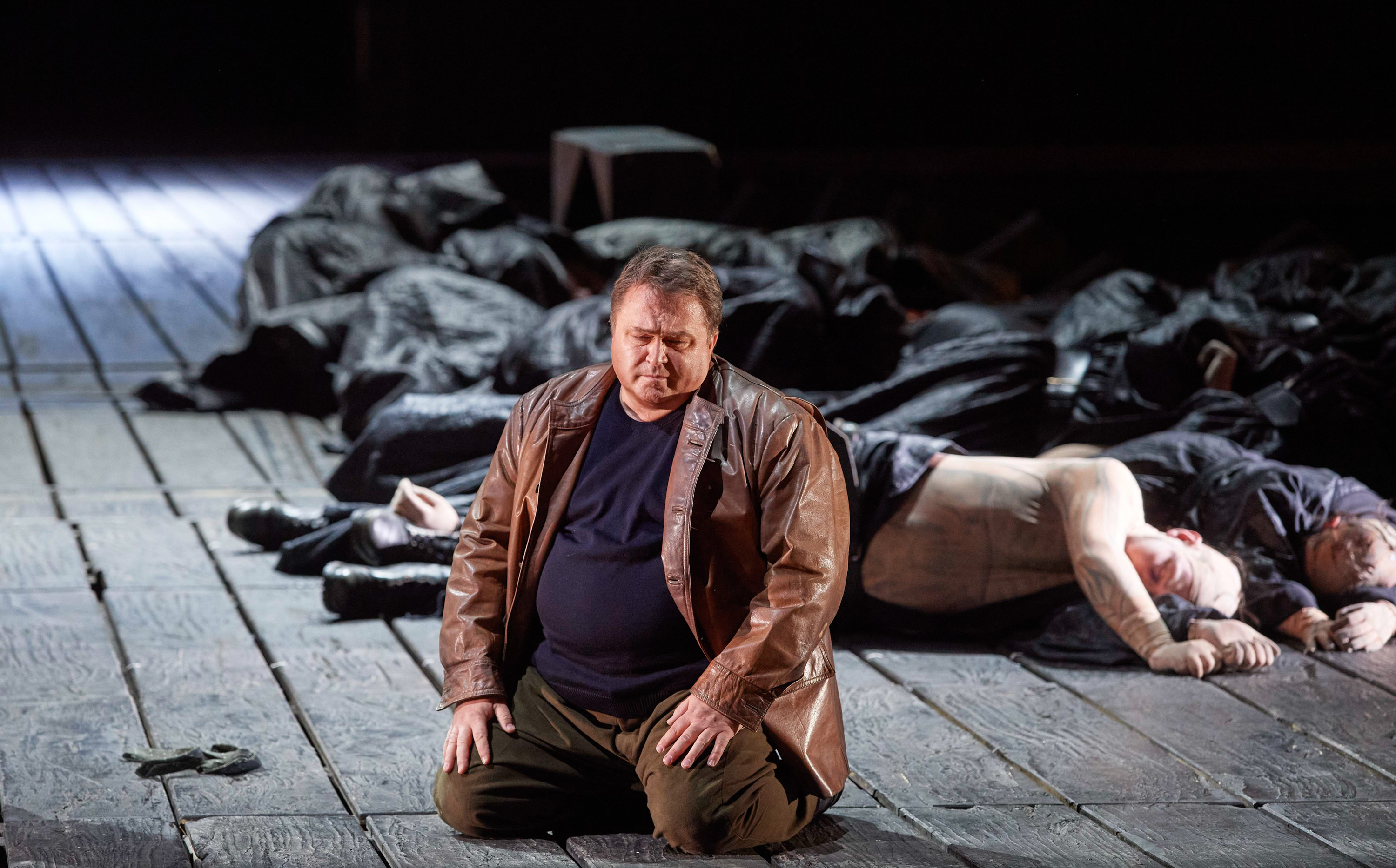 Ein Mann in Lederjacke kniet auf einem Holzboden und blickt verzweifelt nach vorne..