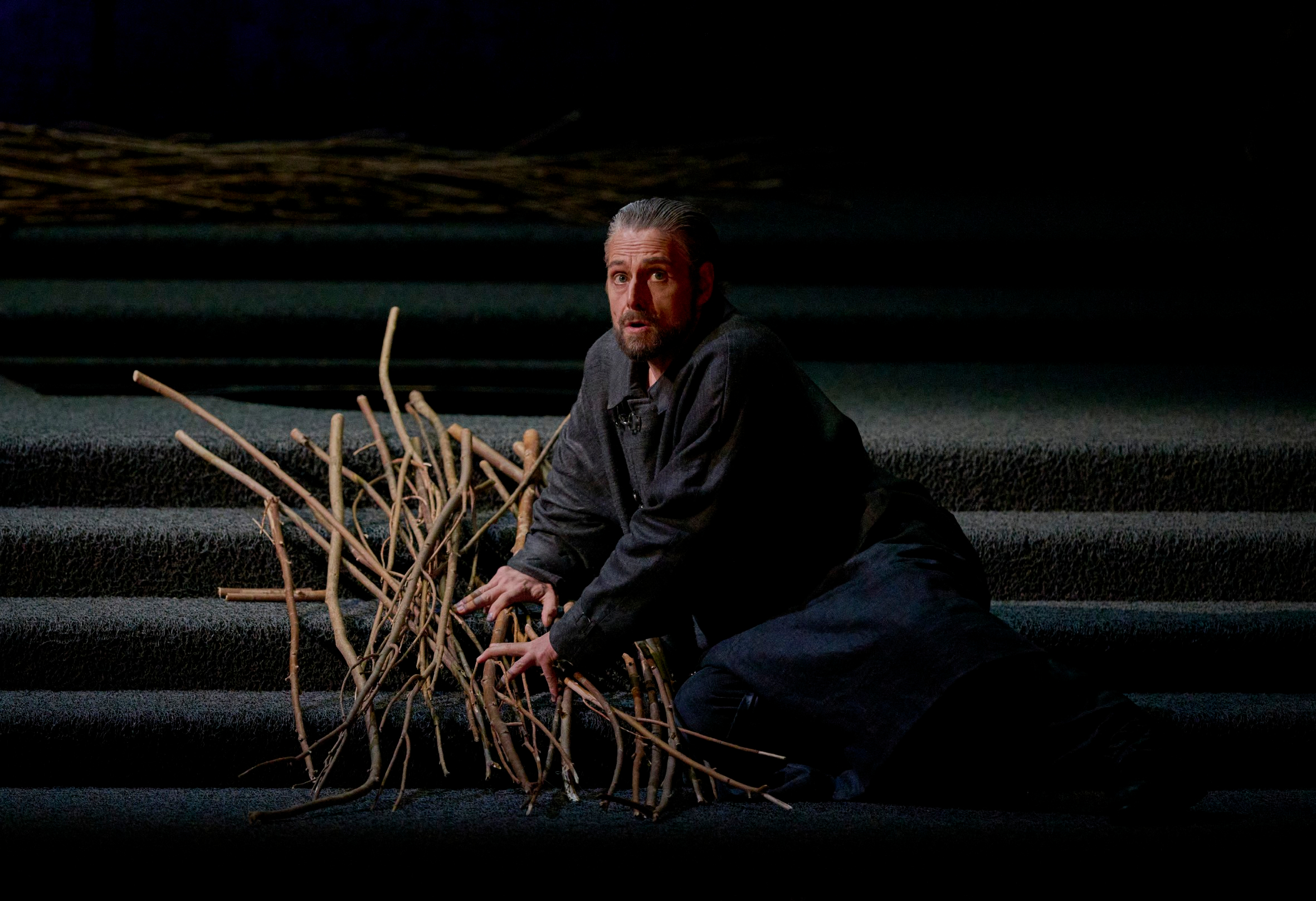 Ein Mann kniet auf einer dunklen Treppe und sammelt besorgt eine große Menge trockener Zweige.