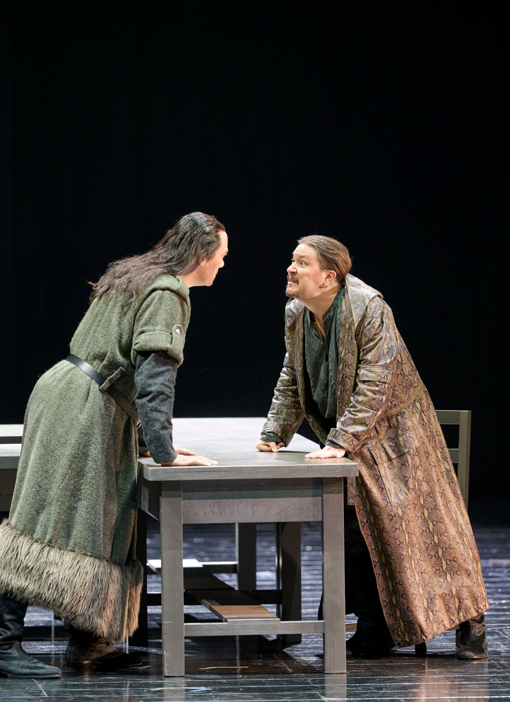 Zwei Männer beugen sich einander wütend über einen Tisch entgegen.