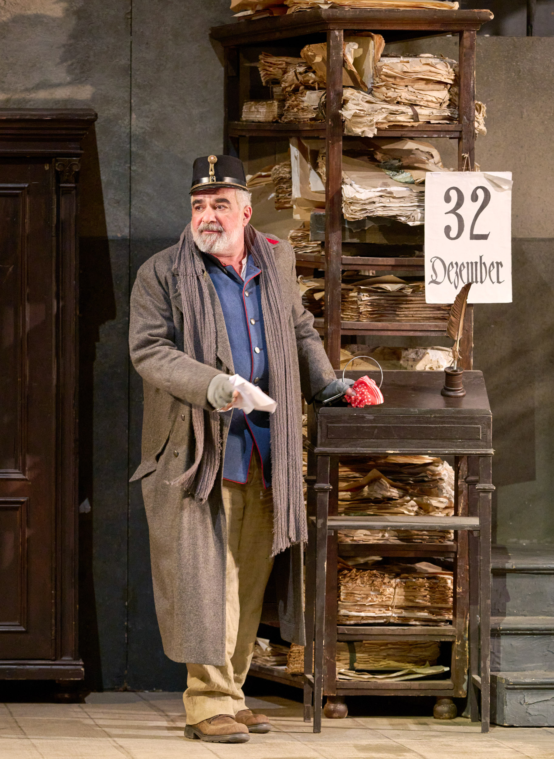 Ein älterer Mann in Uniform steht vor einem großen Stapel Papierstapel und einem Kalenderblatt mit der Aufschrift „32. Dezember“.