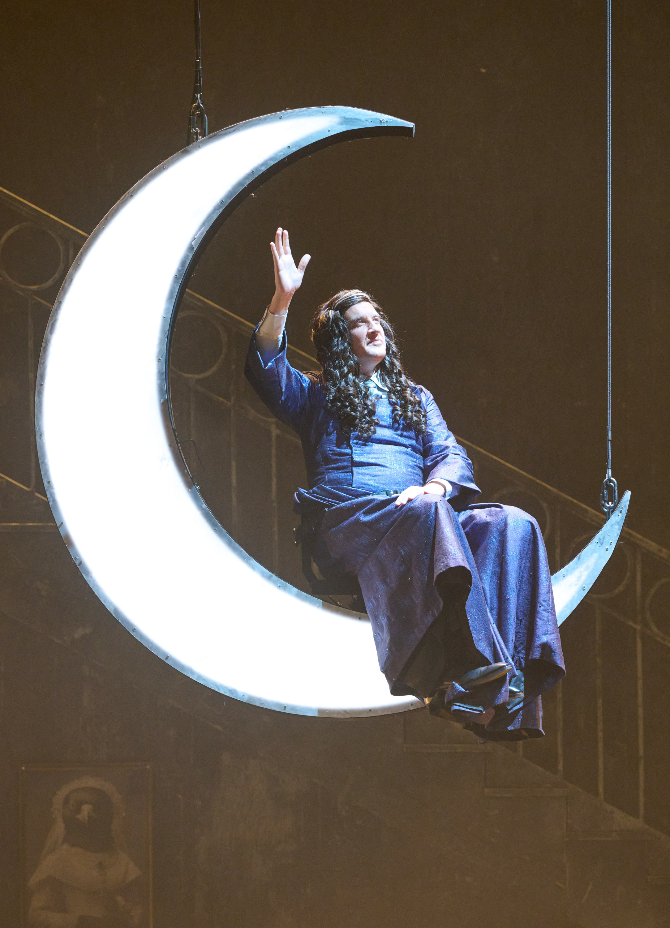 Eine Person mit langen Haaren sitzt in einem langen dunkelblauen Kleid auf einem in der Luft schwebenden Sichelmond.