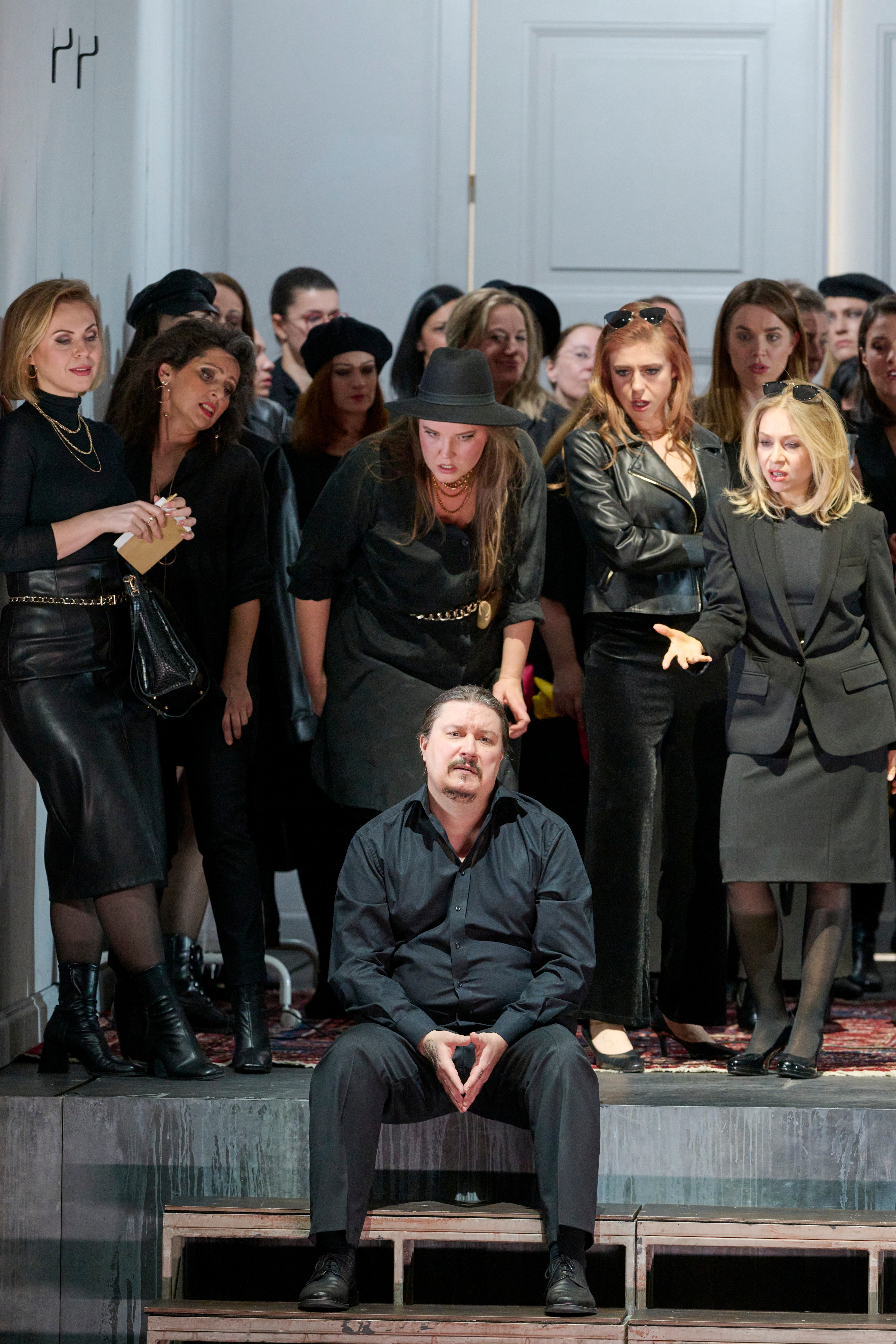 Ein Mann sitzt verzweifelt auf dem Boden, umringt von einer Gruppe schwarz gekleideter Frauen, die ihn emotional ansprechen.