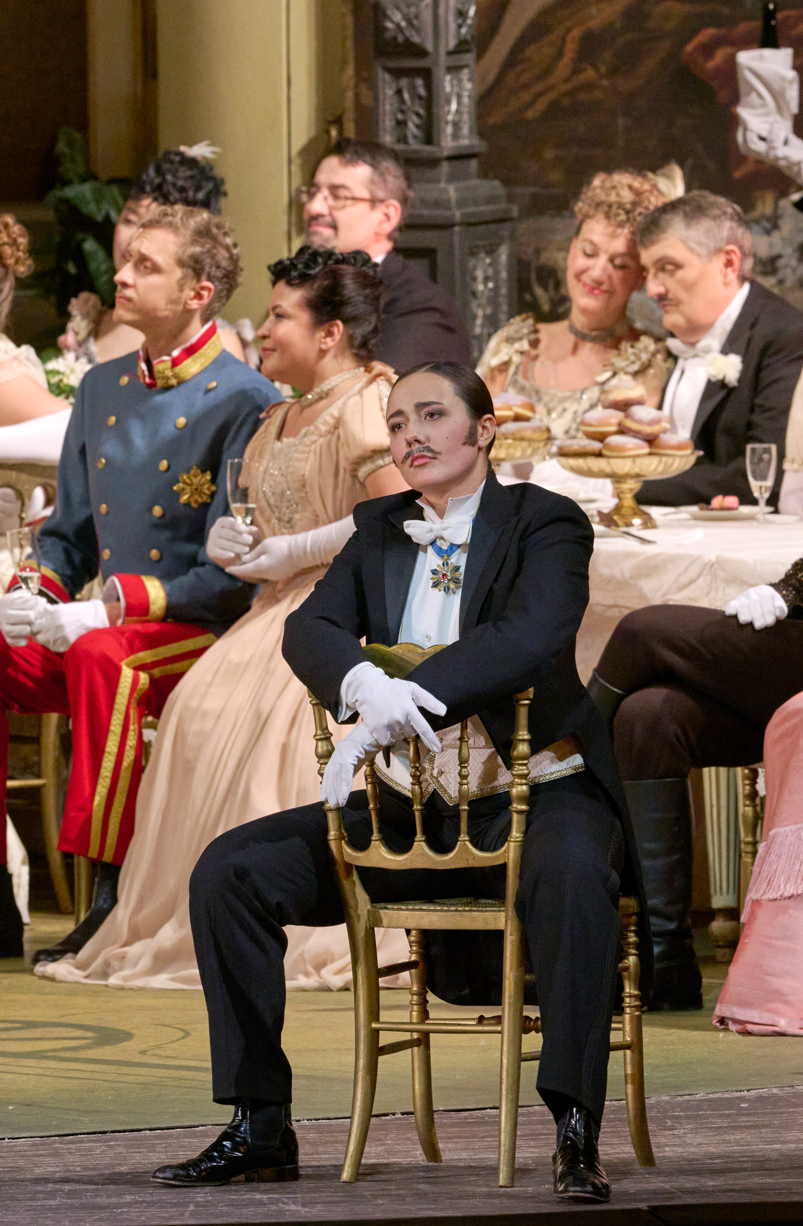 Elegant gekleidete Gäste sitzen dicht beisammen an festlich gedeckten Tischen und verfolgen aufmerksam eine Darbietung.