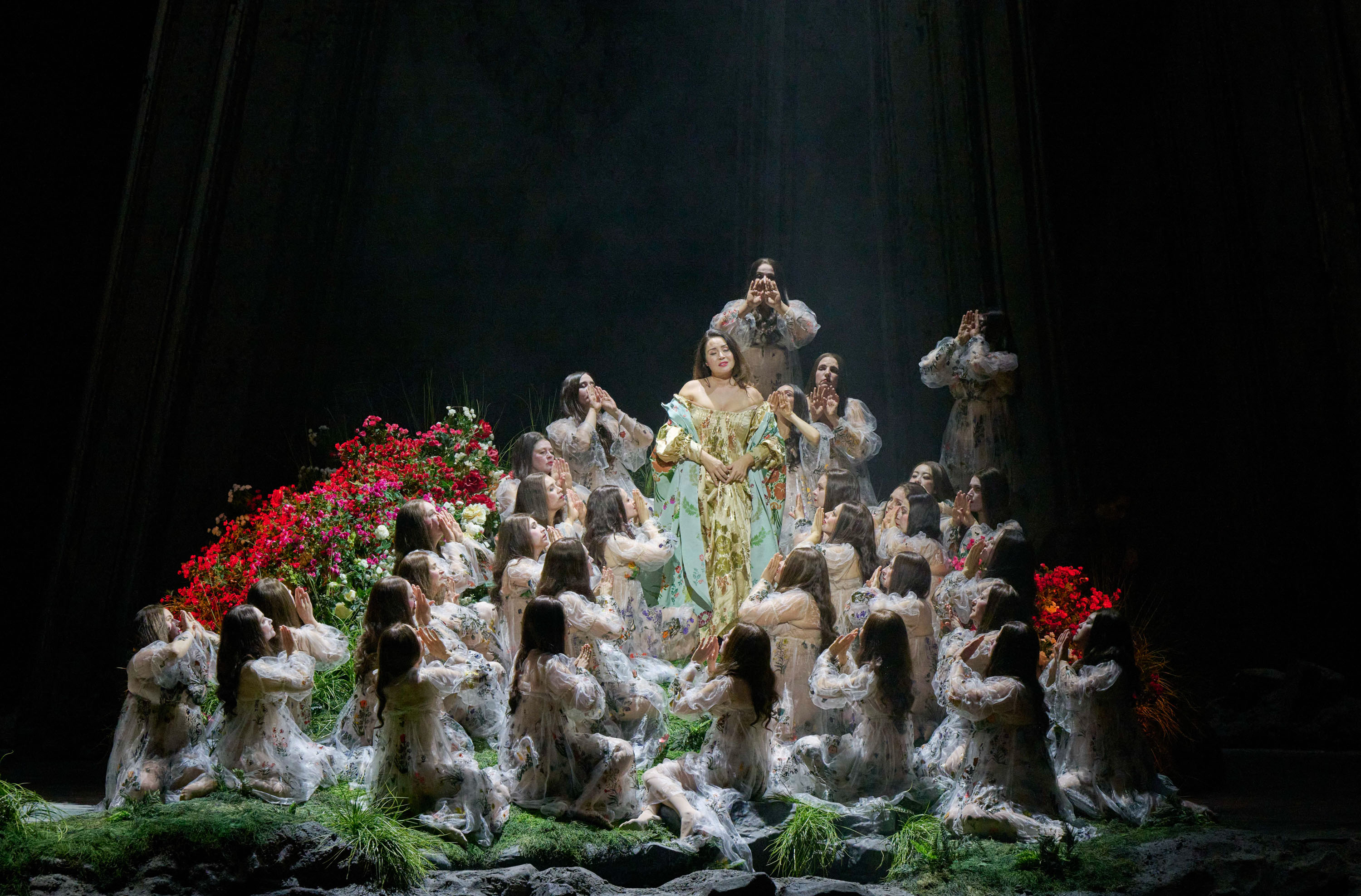 Eine prächtig gekleidete Frau steht erhöht im Zentrum, umgeben von knieenden Gestalten in transparenten Gewändern und leuchtend roten Blumen.