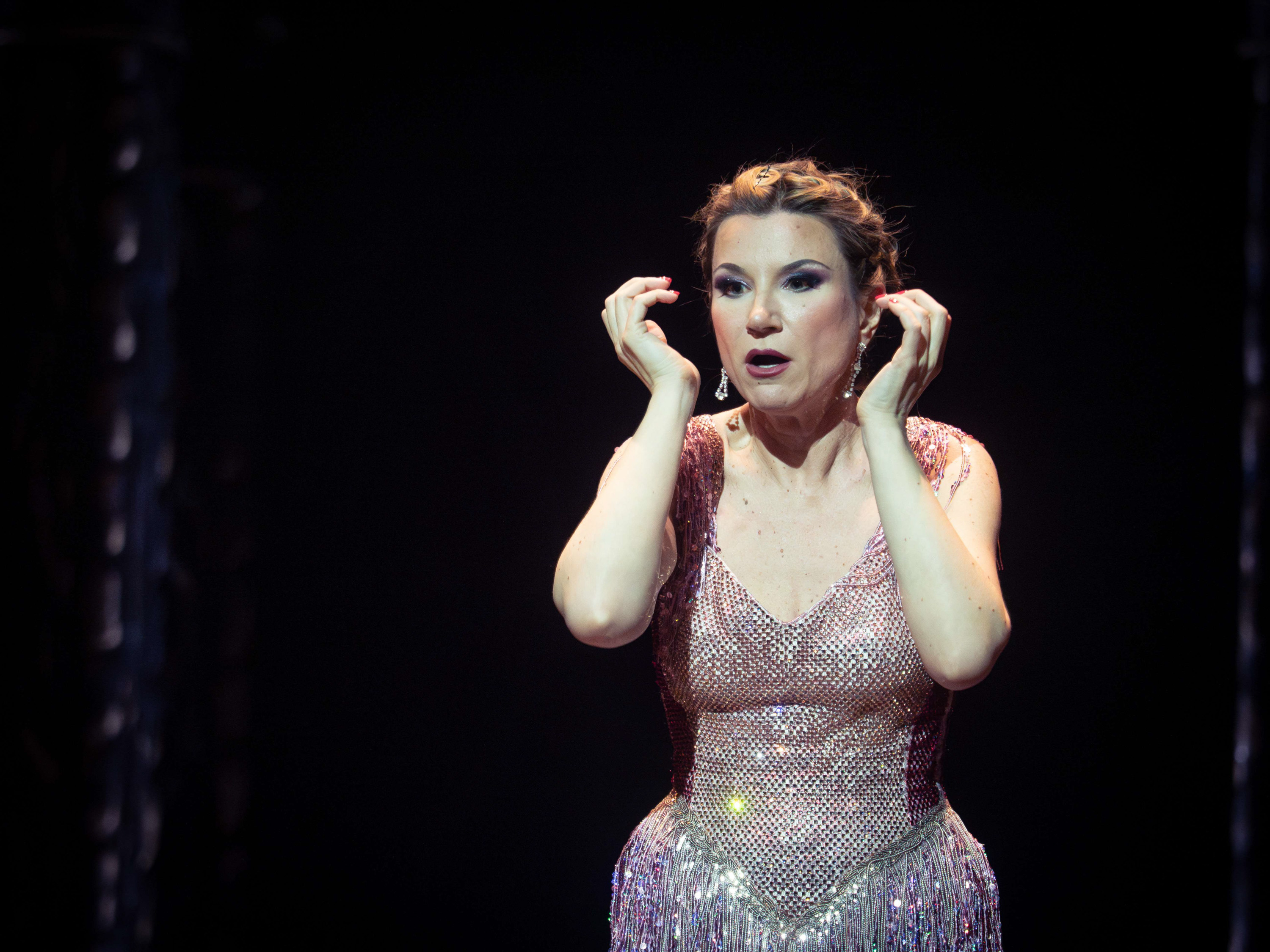 Eine Frau in einem Rosa Glitzerkostüm steht vor einem schwarzen Hintergrund.