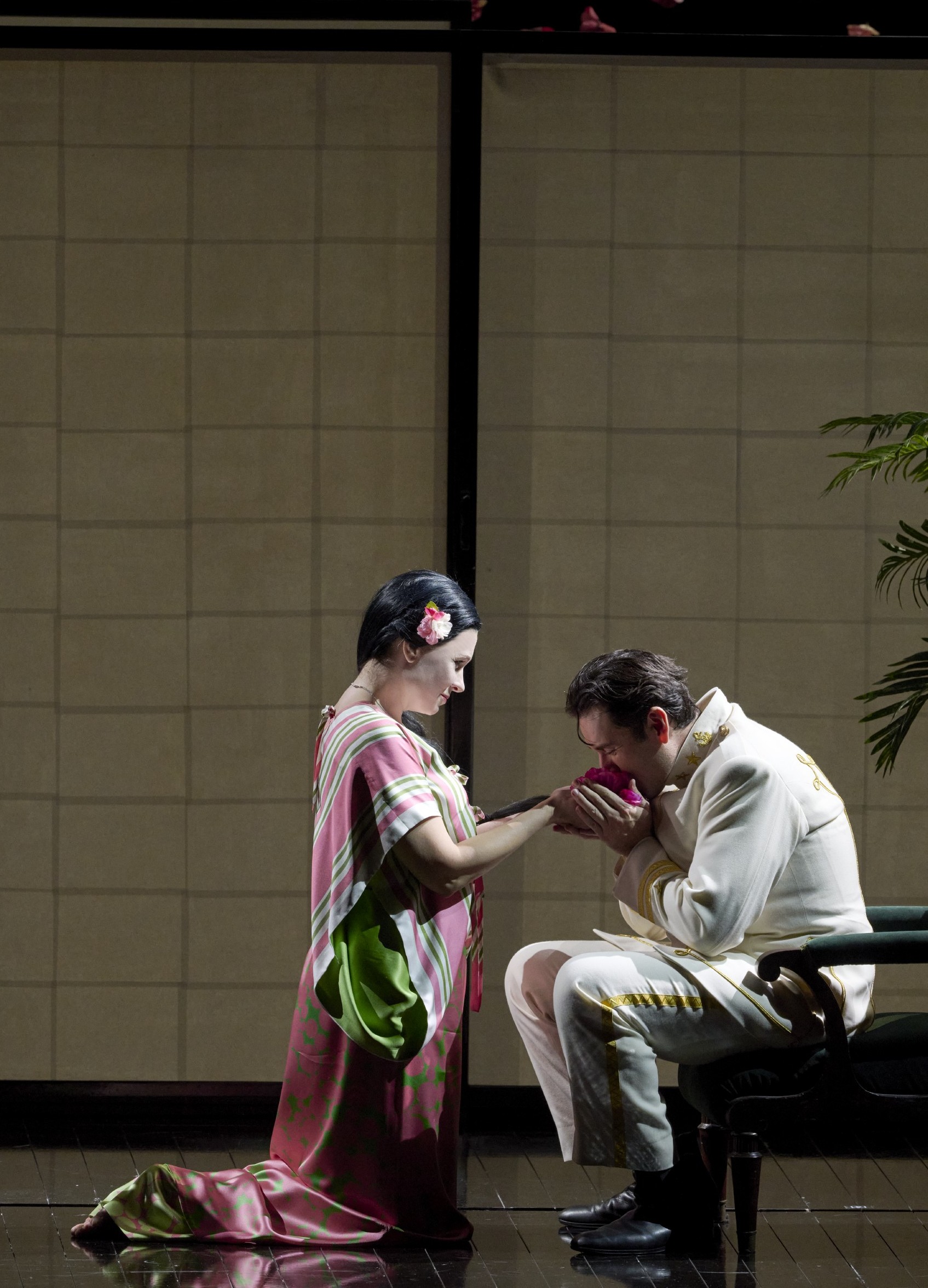 Ein Mann in weißer Uniform kniet vor einer Frau im Kimono und küsst ihre Hand in einer zärtlichen Geste.