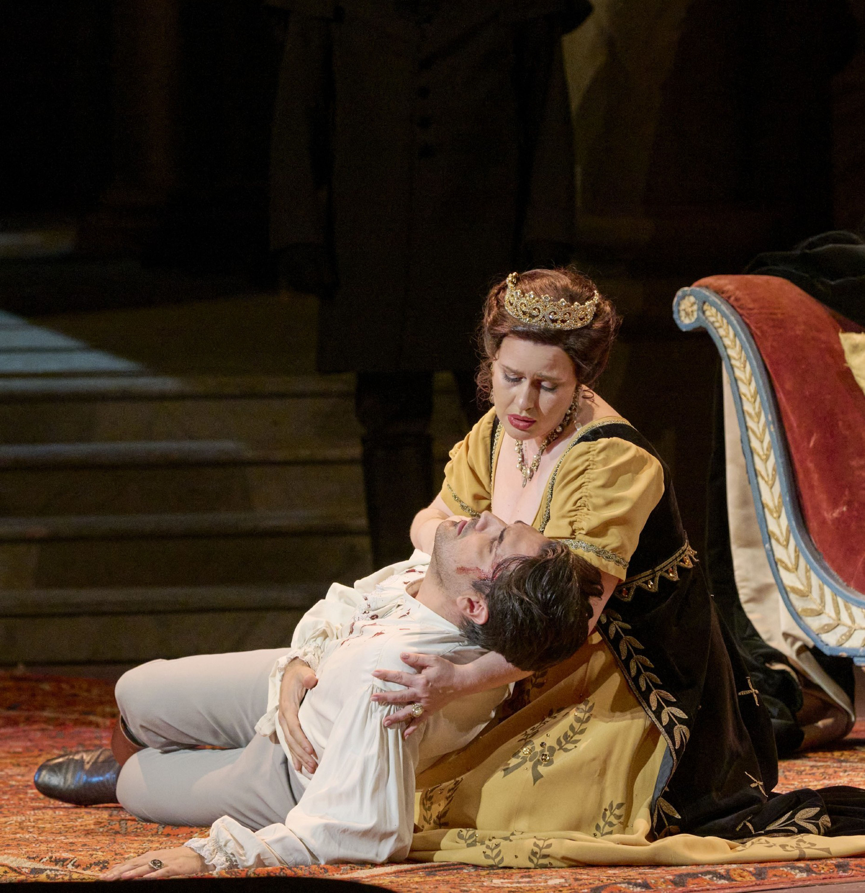 Eine Frau mit einer Krone auf dem Kopf kniet am Boden. In ihren Armen hält sie einen blutverschmierten Mann.