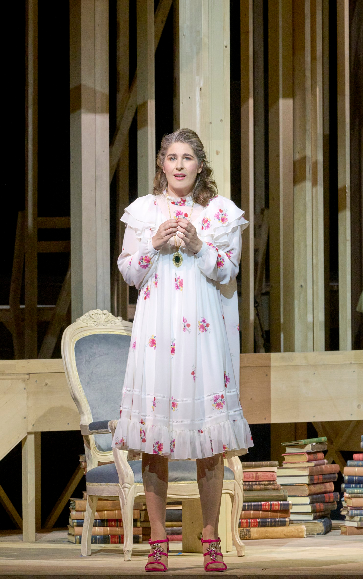 Eine Frau im weißen Nachthemd mit Blumenmuster steht singend vor einer hölzernen Bühnenkonstruktion.