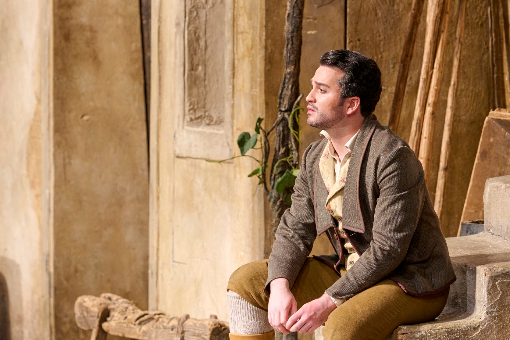 Ein Mann in historischer Kleidung sitzt nachdenklich auf einer Treppe vor einer mediterranen Hausfassade.