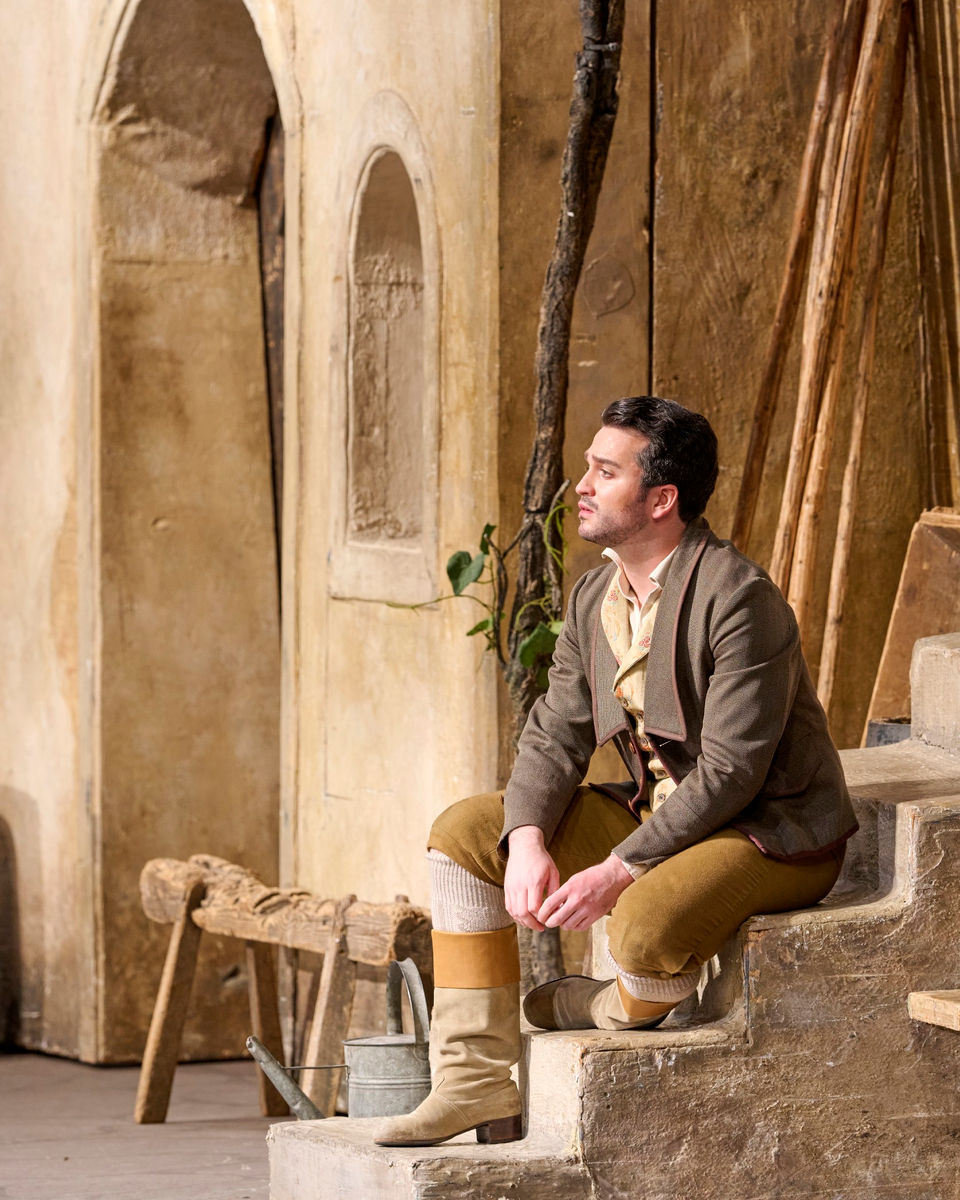 Ein Mann in historischer Kleidung sitzt nachdenklich auf einer Treppe vor einer mediterranen Hausfassade.