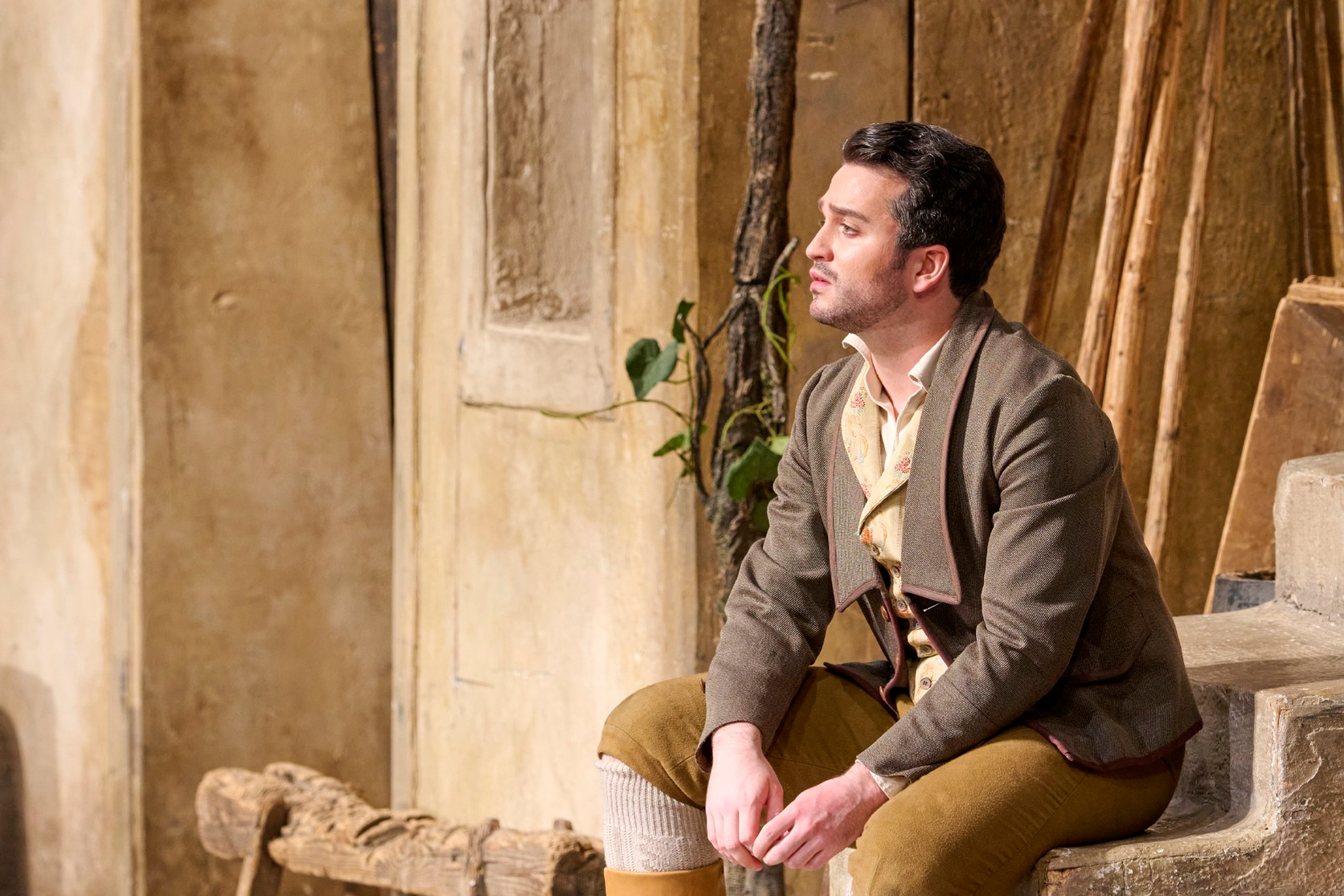 Ein Mann in historischer Kleidung sitzt nachdenklich auf einer Treppe vor einer mediterranen Hausfassade.