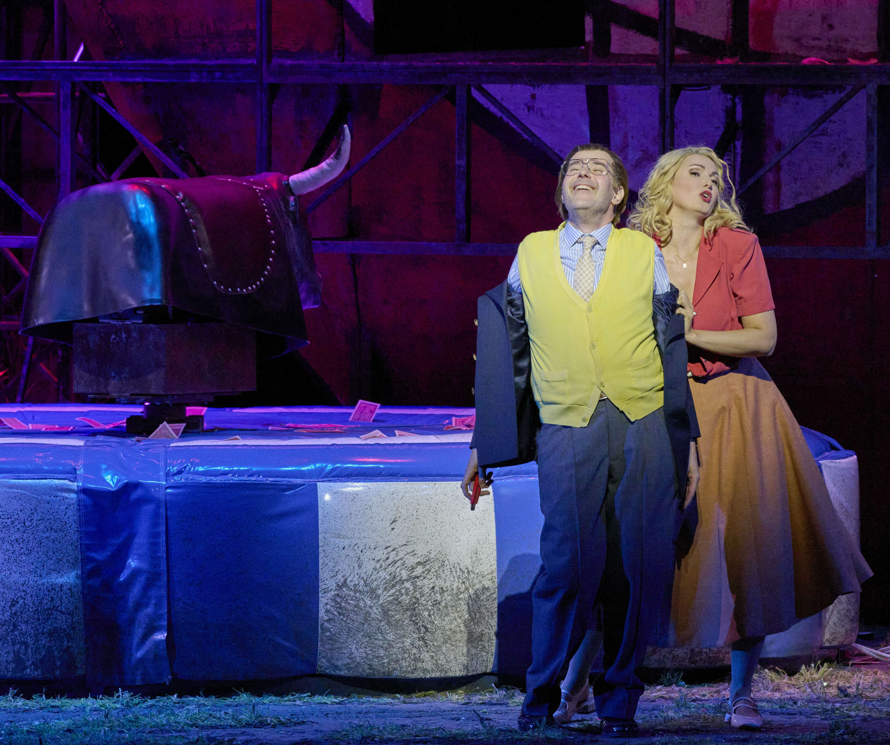 Ein Mann und eine Frau stehen gemeinsam vor einem mechanischen Bullen. Beide sind bunt gekleidet.