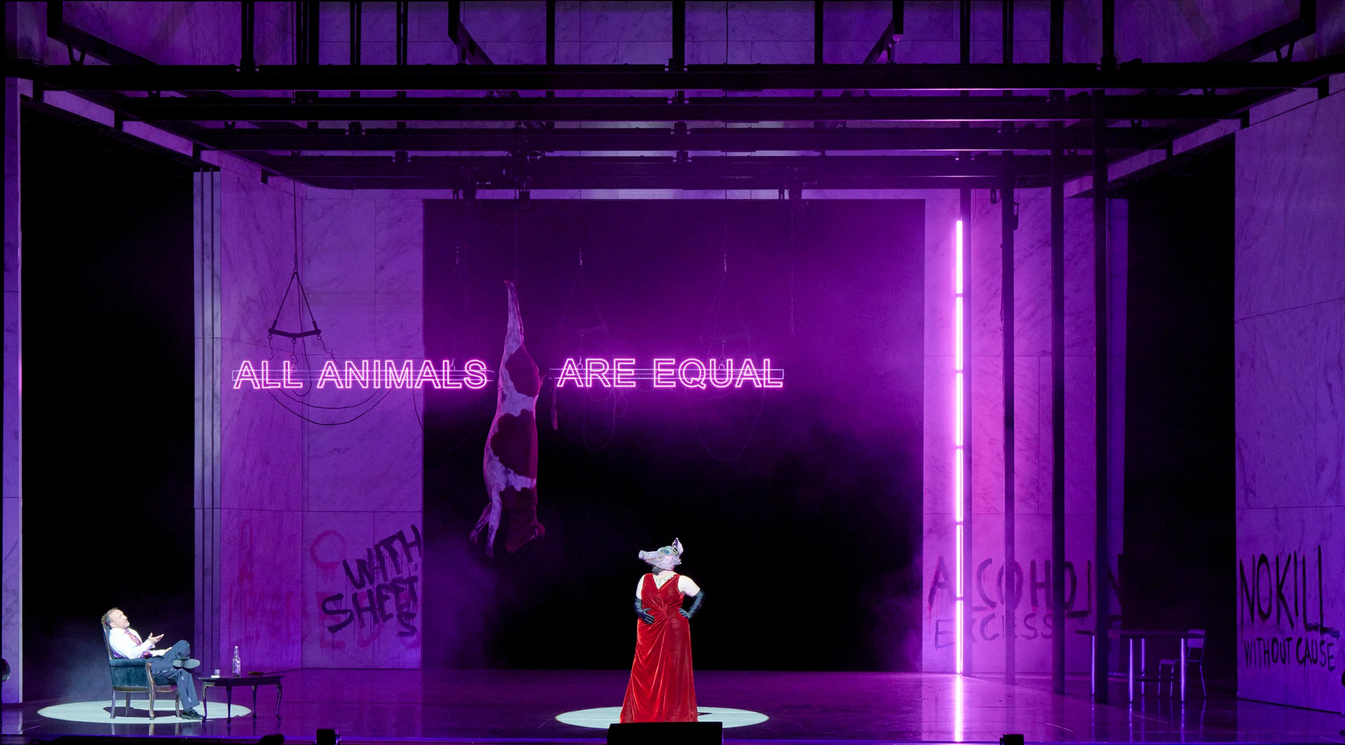 Eine Figur mit Schweinemaske steht in rotem Gewand im Zentrum einer lila beleuchteten Bühne, hinter ihr leuchtet der Satz „ALL ANIMALS ARE EQUAL“.