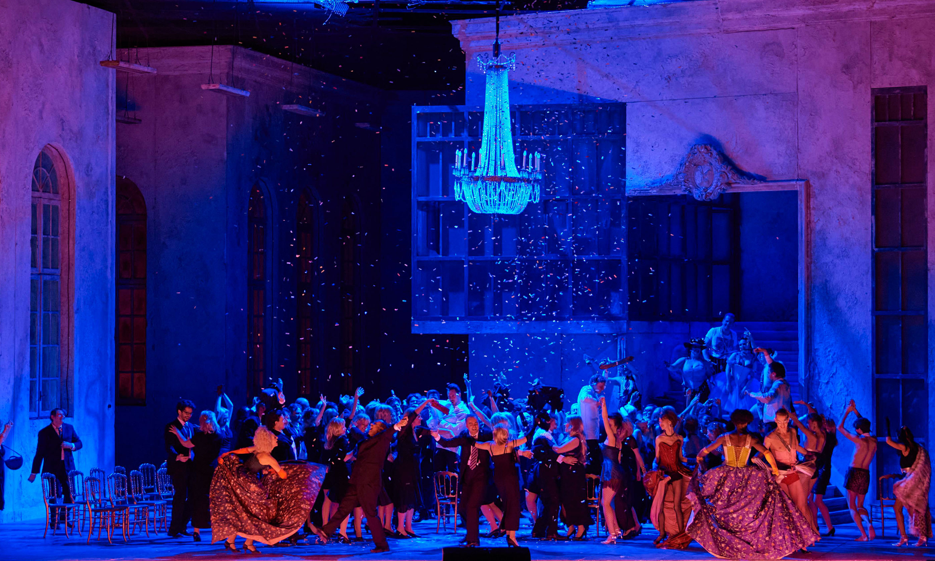 Eine große Menschenmenge feiert und tanzt ausgelassen in einer Bühnenkulisse