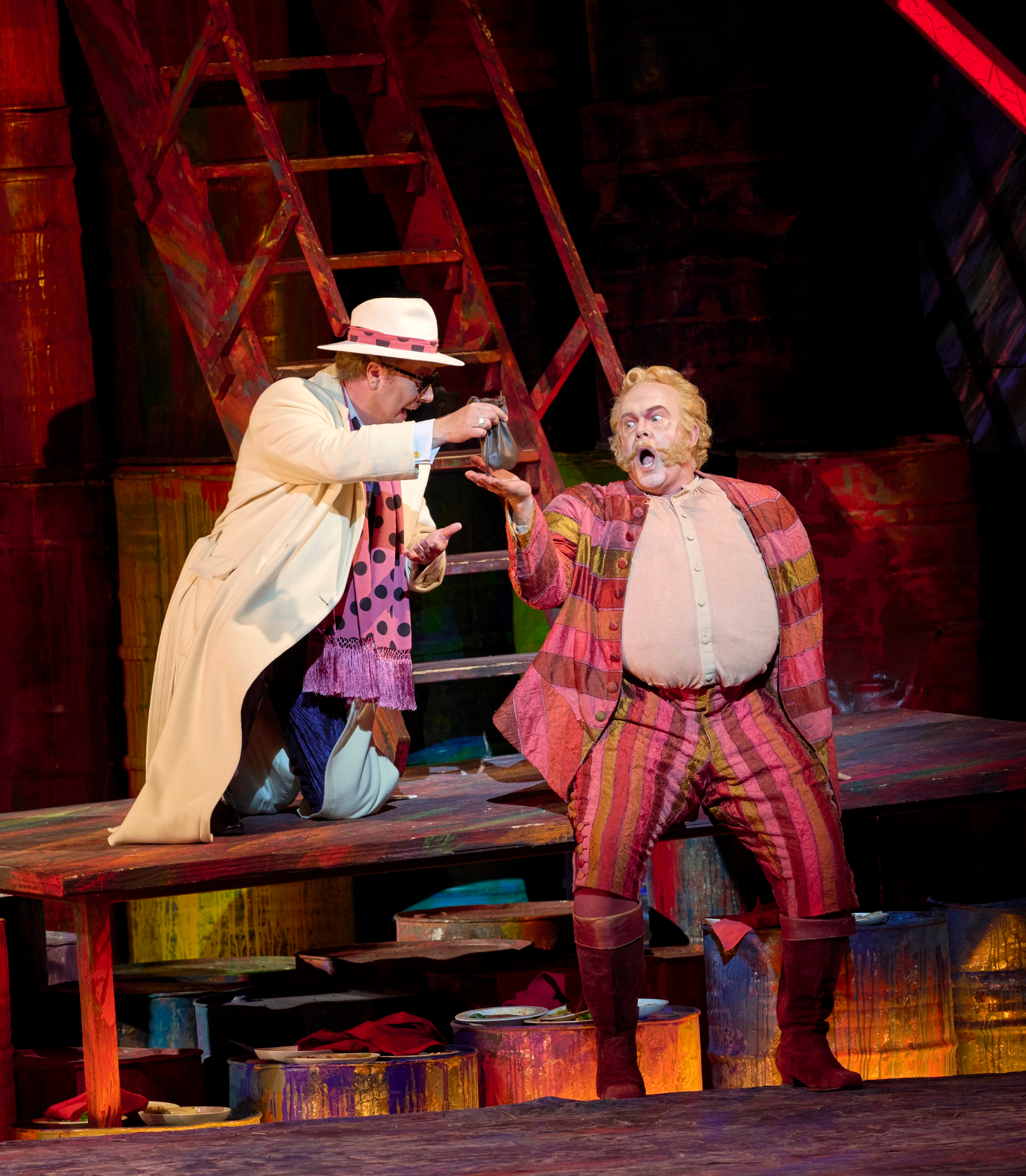 Zwei Darsteller in bunten Kostümen spielen eine dramatische Szene auf einer farbenfrohen Bühne.