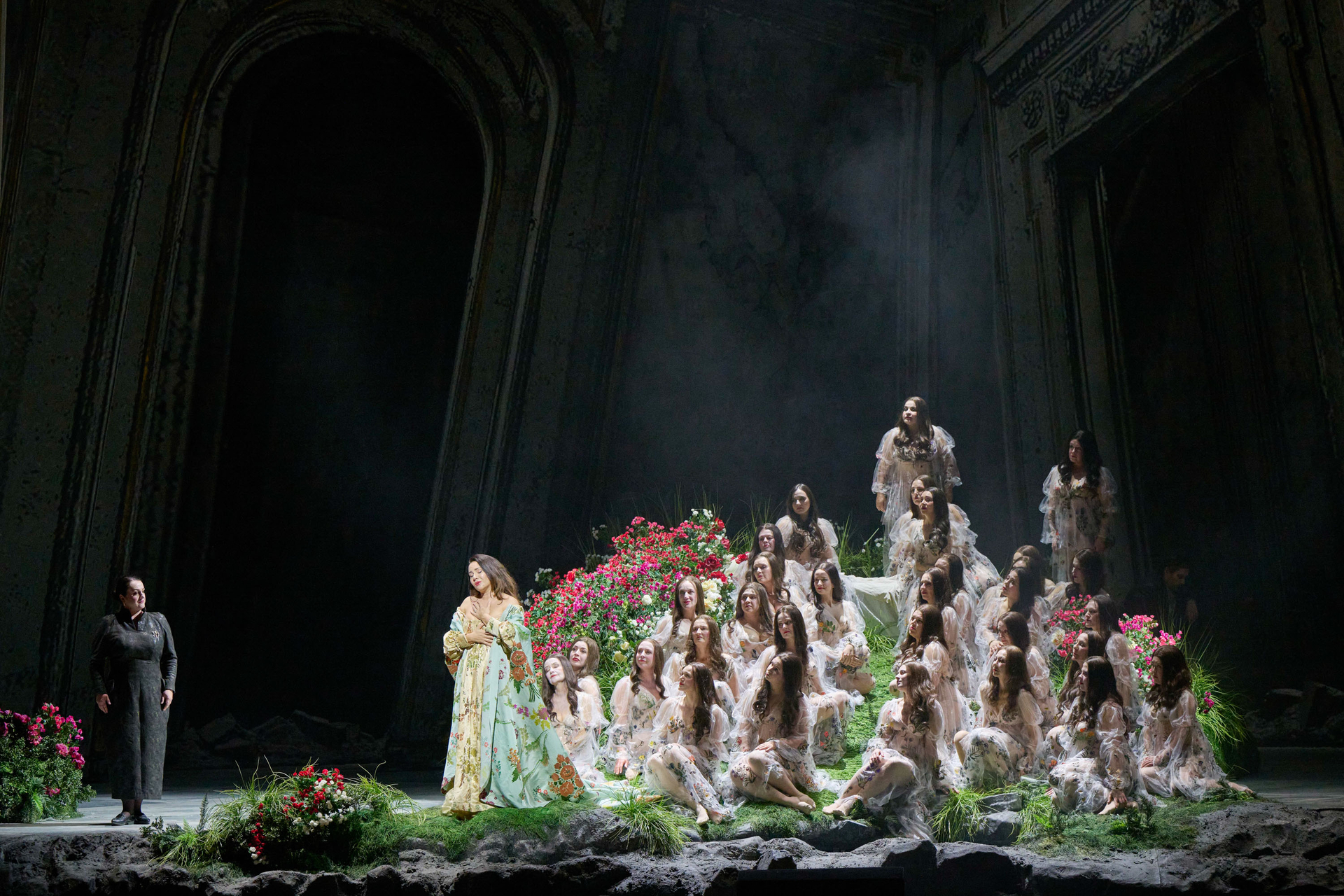 Eine in Gold und Türkis gekleidete Figur steht links auf einer mystischen Blumenbühne, rechts gruppieren sich zahlreiche weiß gekleidete Gestalten auf Terrassen.