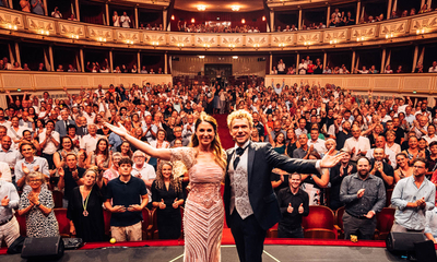 Ein Mann und eine Frau stehen auf der Bühne der Wiener Staatsoper; im Hintergrund ist der volle Publikumssaal zu sehen.