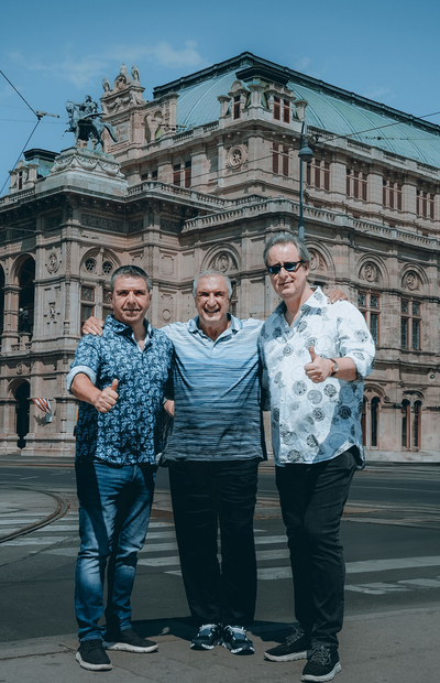 Drei Männer posieren vor dem Gebäude der Wiener Staatsoper 