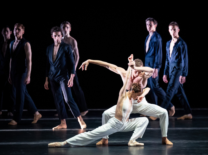 Ballettpaar tanzt während sie im Hintergrund von Personen beobachtet werden.