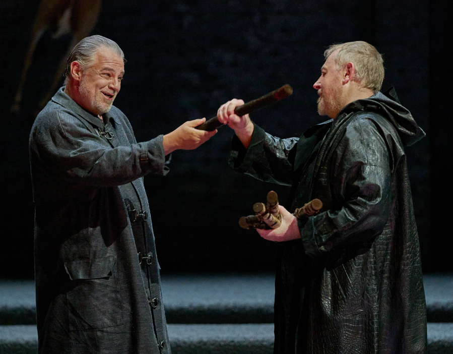 Zwei Männer in dunklem Gewand stehen sich gegenüber; der eine überreicht dem anderen einen Stab.