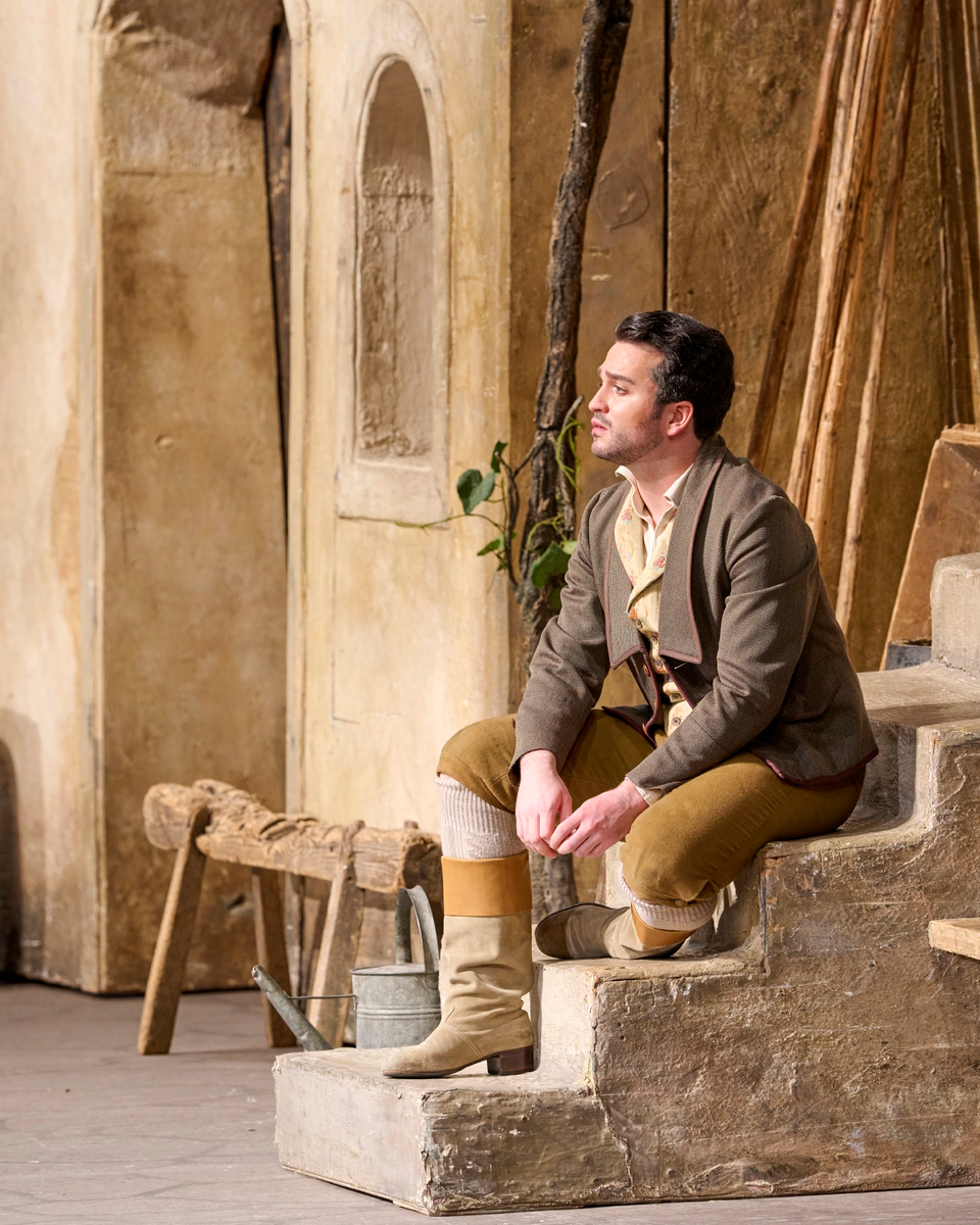 Ein Mann in historischer Kleidung sitzt nachdenklich auf einer Treppe vor einer mediterranen Hausfassade.